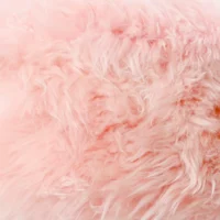 Close-up of soft, fluffy pink sheepskin fur with varying shades and textures. The plush strands create a cloud-like, cosy appearance—an inviting expanse of pastel pink with dreamy waves and depth.