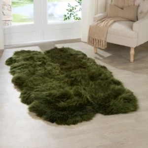 A green quad sheepskin rug with an irregular shape rests on a light wood floor in a sunlit room, beside a beige armchair draped with a tan throw, as sunlight pours through white-framed glass doors.