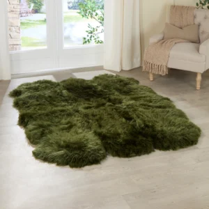 A Green 6 pelt Sheepskin Rug with a natural hide shape lies on a light wood floor in a bright room. Nearby, a beige armchair with a knitted throw sits by sheer curtains framing glass doors that reveal greenery outside.