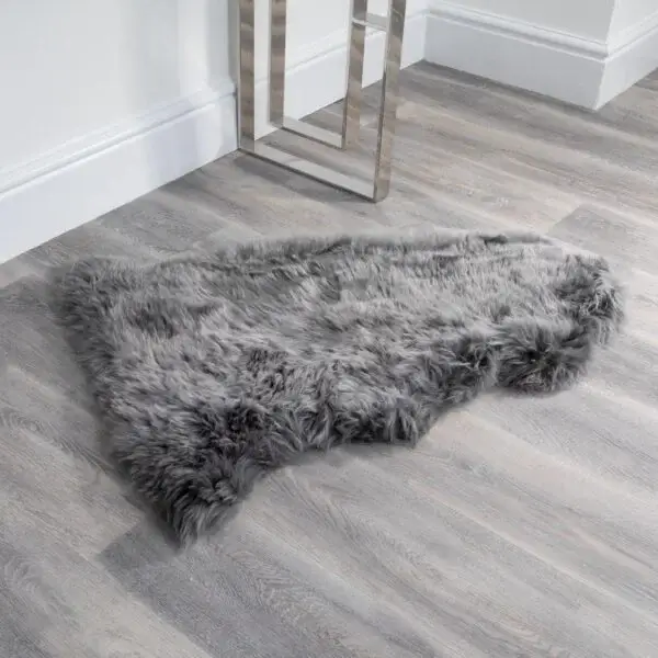 An Extra Large Grey Sheepskin Rug with an organic hide shape rests on light wood flooring by a white wall and a modern metallic table, adding a cosy accent to the room’s corner.