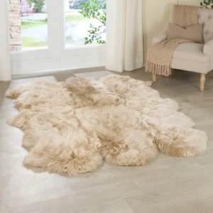 A Champagne 6 Pelt Sheepskin Rug with a plush, irregular shape rests on a light wood floor. Nearby, a beige upholstered chair with coordinating throw faces tall windows with white curtains, revealing greenery outside.