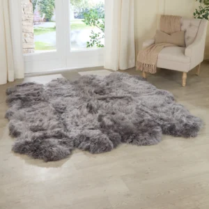 The Grey Octo Sheepskin Rug rests on a light wooden floor in a sunlit room with a beige armchair, tan throw, and white-curtained glass doors opening to a green garden.