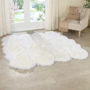 A Natural White Octo Sheepskin Rug is spread over a light wooden floor by glass doors. Close by, a beige armchair with a tan throw sits, while cream curtains frame the outside greenery. British spelling applied: A Natural White Octo Sheepskin Rug is spread over a light wooden floor by glass doors. Close by, a beige armchair with a tan throw sits, whilst cream curtains frame the outside greenery. *(Note: The original text already largely follows British conventions. Whilst can be used instead of while for extra British flavour.)*.