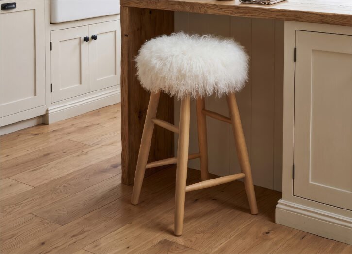White curly sheepskin wooden stool sat at a kitchen island in a country style kitchen.