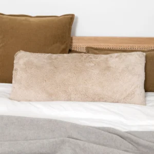 Champagne beige long shearling sheepskin cushion on a bed with white bedding and brown velvet pillows.