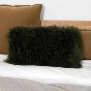 Forest green rectangular Mongolian sheepskin cushion with long curly pile on a bed, in front of a tan velvet pillow.